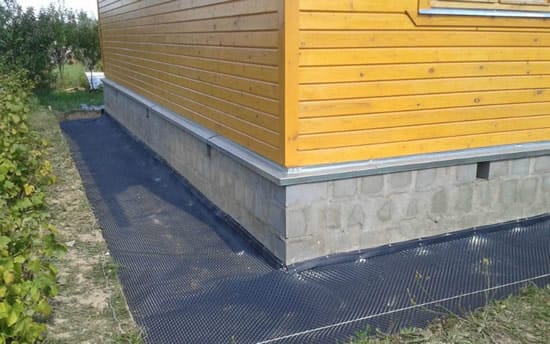 На дно траншеи укладывают гидроизоляционную пленку с нахлестом на дом