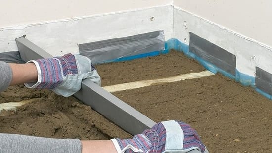 Процесс выравнивания цементной стяжки с помощью правила